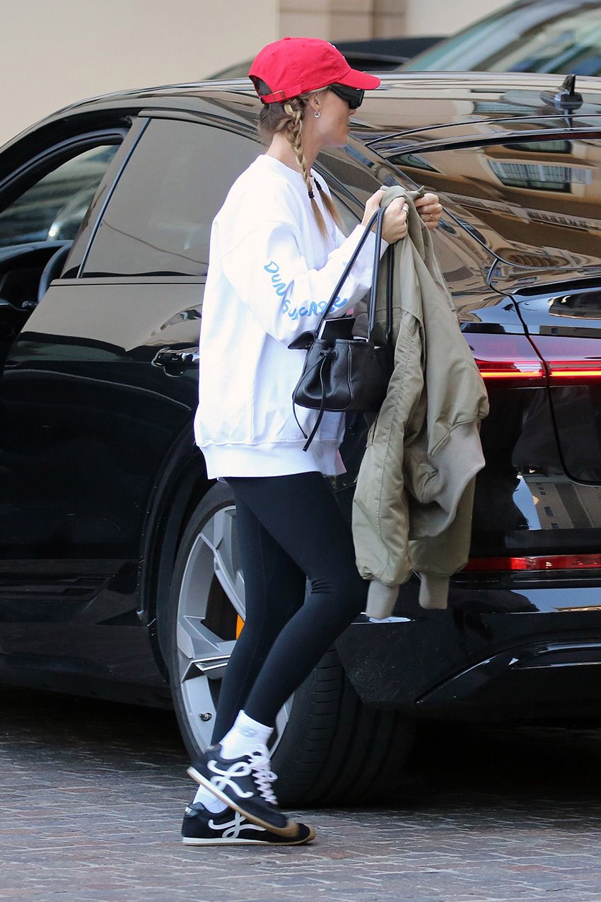 Margot Robbie in L.A. wearing a red baseball cap, white sweatshirt, black leggings, and Loewe Flow Runner sneakers
