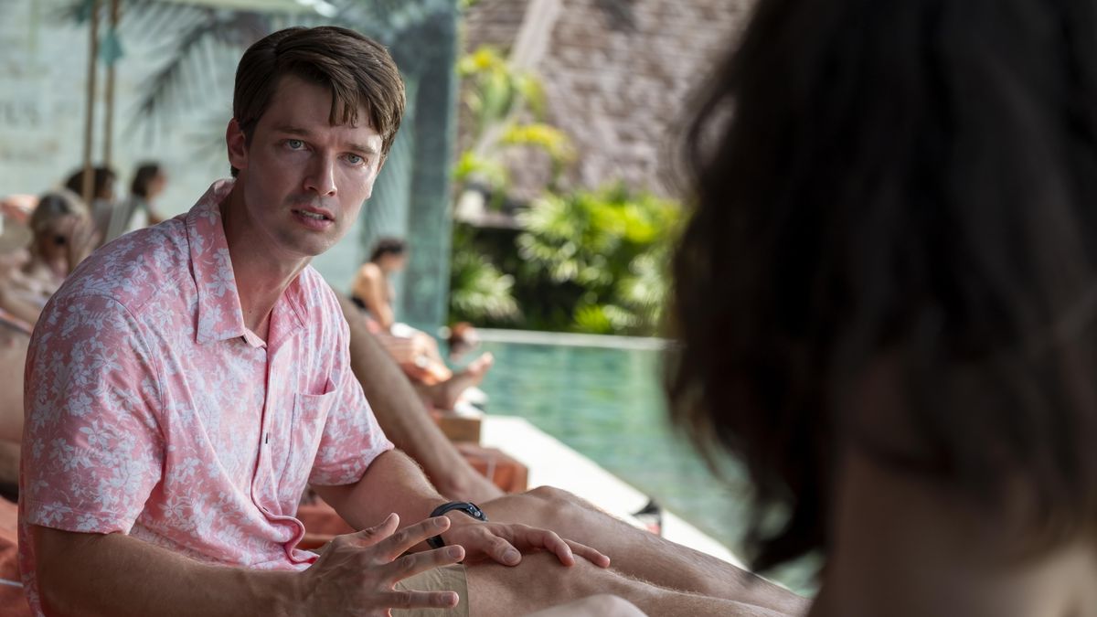 Saxon in a pink shirt, sitting on a lounger by a pool and looking shocked 