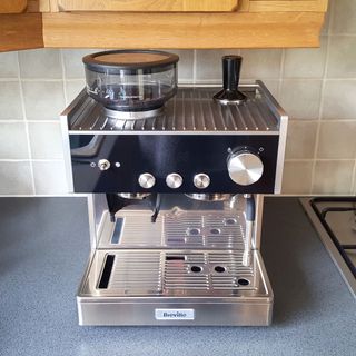 The Breville Barista Signature Espresso Machine in a kitchen with a grey granite worktop and oak wall cupboards