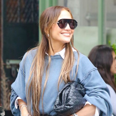 Jennifer Lopez in NYC wearing a blue sweatshirt over a white collared shirt with wide-leg jeans and mesh high-heel mule sandals, carrying a Bottega Veneta woven clutch