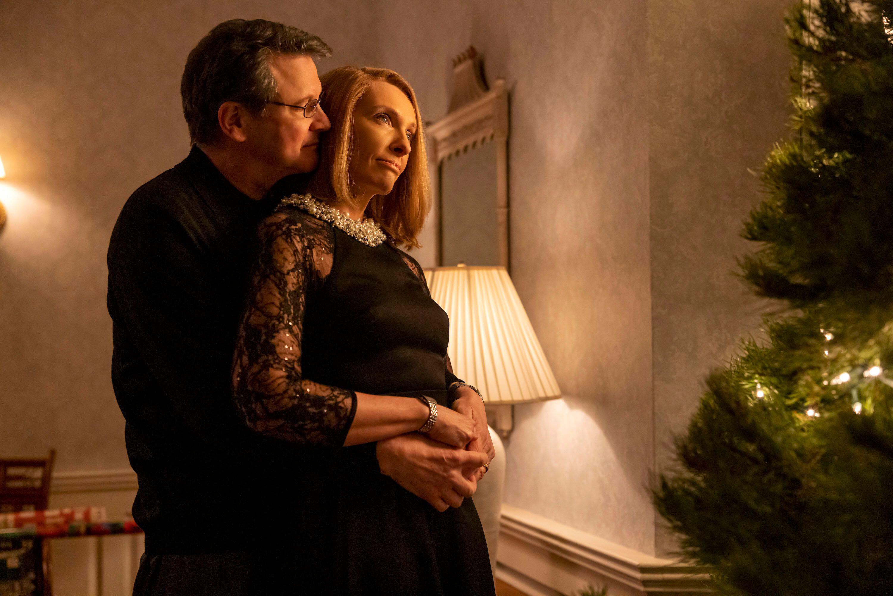 colin firth hugs toni collette from behind as they look at a christmas tree in the staircase