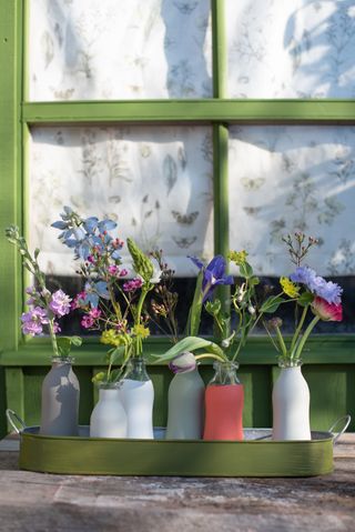 colourful vases painted in garden paint and filled with flowers on a green window ledge