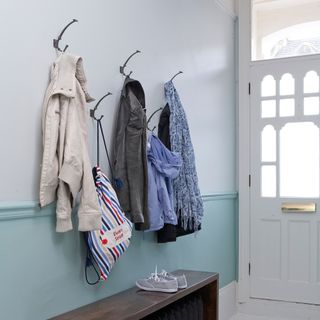 Pale blue and white narrow hallway with three coats hanging up on wall
