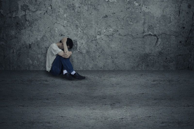 A young man sits alone near a grey wall.