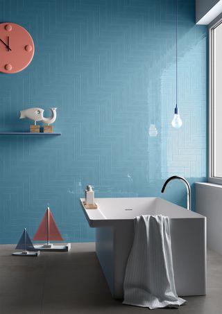 Blue tiled statement wall with minimalist, sleek bathtub and single hanging bulb