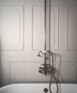 A close up of white bathroom wall panels with a long silver showerhead and faucet on the wall and a white bath underneath