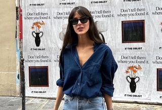 @leiasfez wearing a navy blue button-down shirt with jeans and sunglasses.