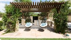 Stone patio space with wooden pergola with greenery and two hammock chairs