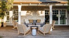 terrace patio off the back of a stone building with white pillars and decking patio area with wooden furniture, rocking chairs and a small blue side table