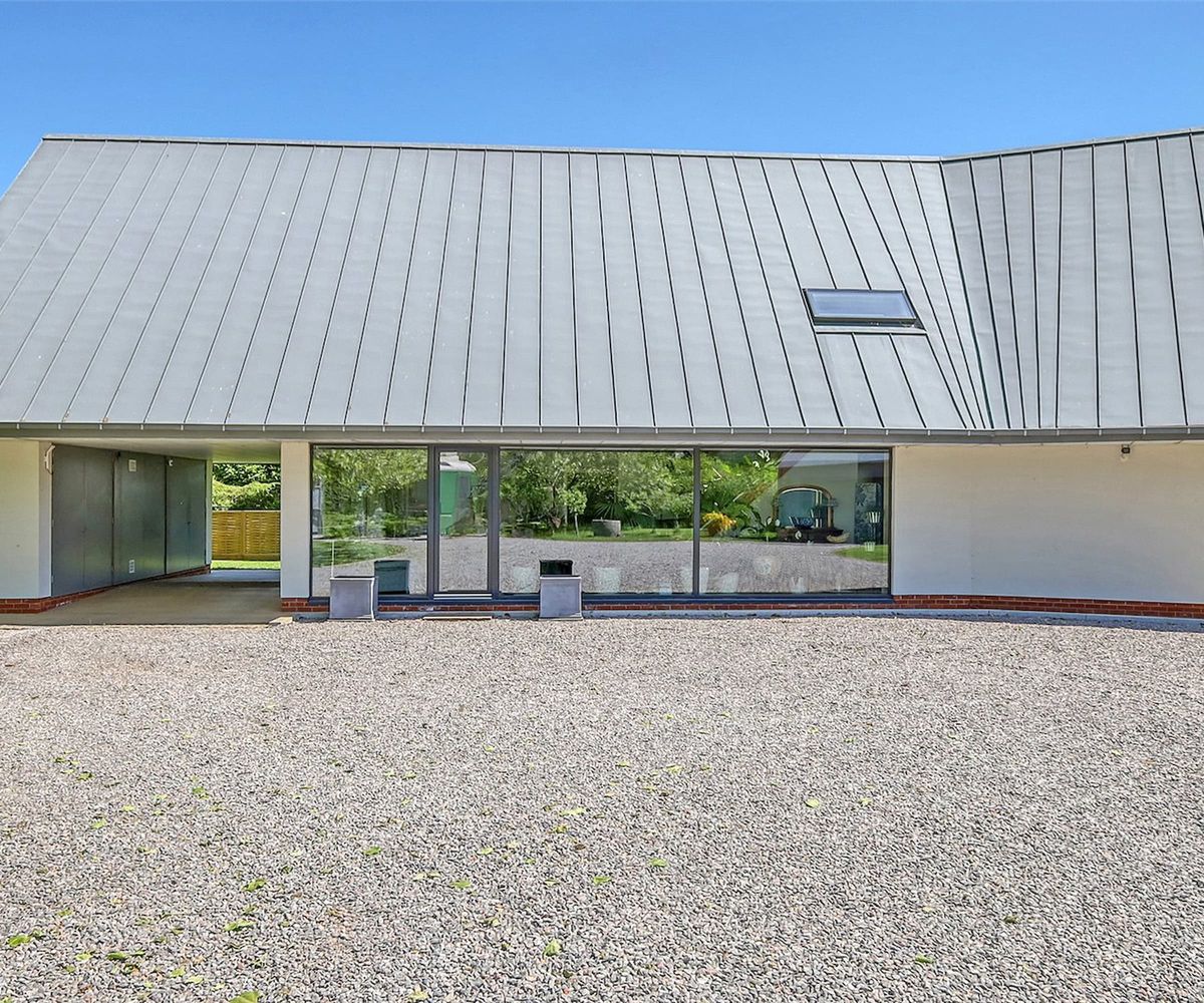 A gravelled driveway next to a grey house with tall glass bifold doors
