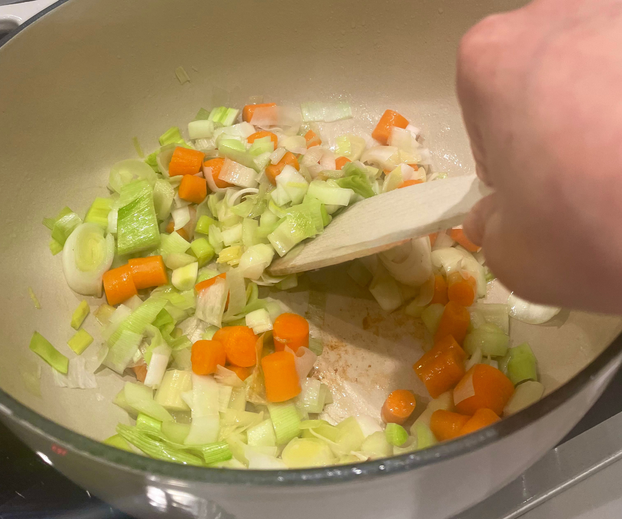 Cooking diced vegetables in the Lodge 6QT Enameled Cast Iron Dutch Oven, stiring with a spatula.