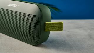 a close-up photo of a carry strap on a green bluetooth speaker made by bose with a clean plastic casing and no visible woofers rests on a table