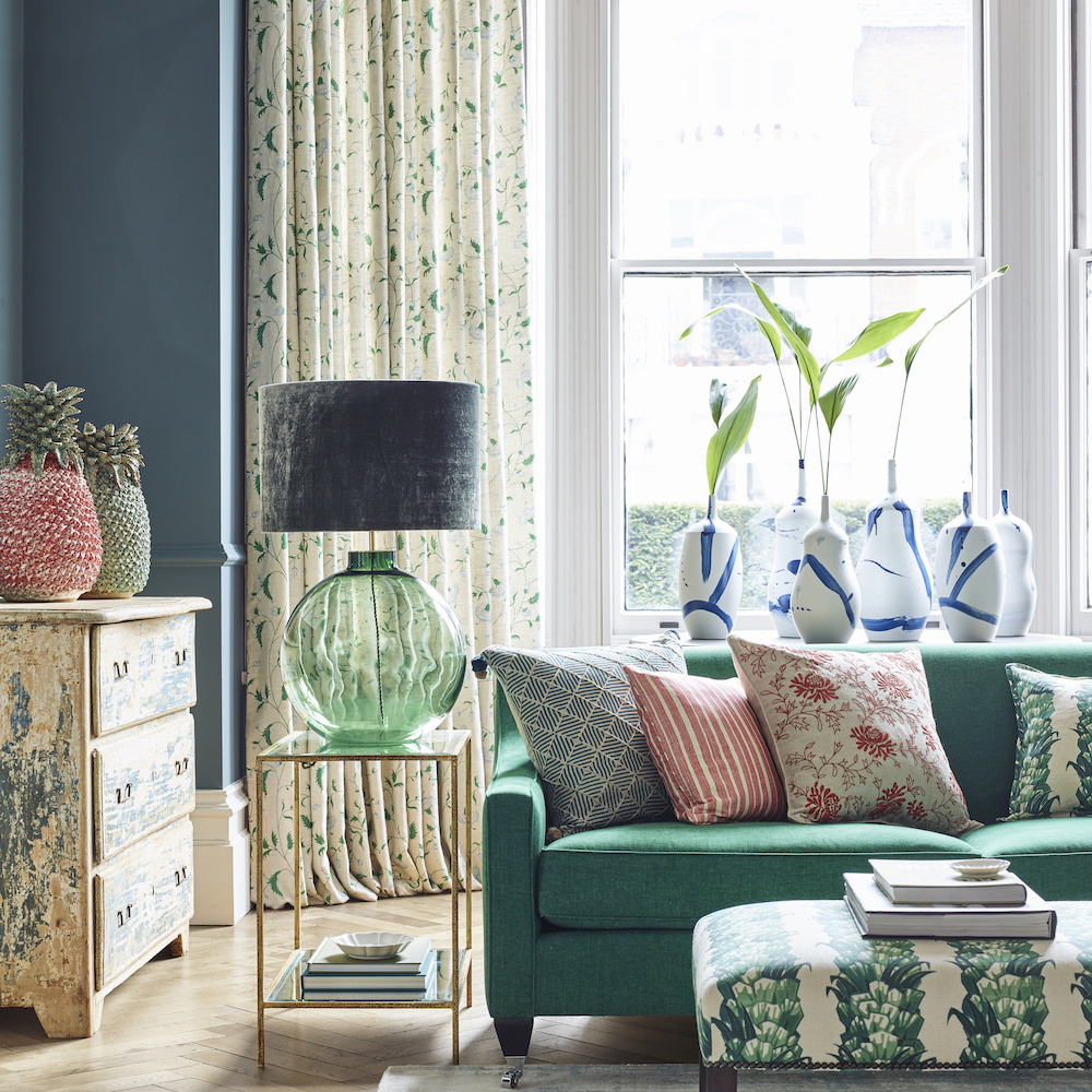 Dark green sofa and patterned green footstool, navy walls and oversized vases in window