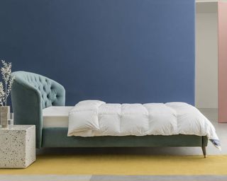A goose down duvet cover laid on a bed with a teal velvet headboard in a contemporary blue bedroom