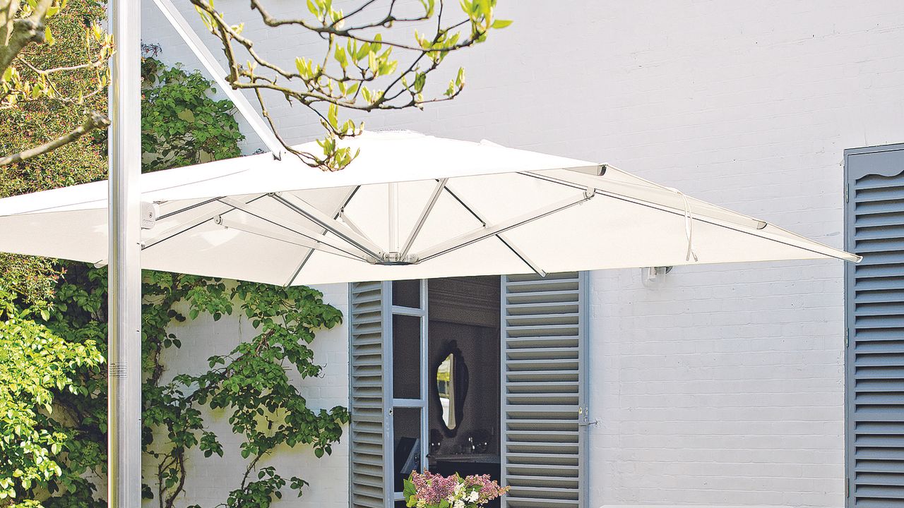 White parasol in garden on top of white dining set with chairs.