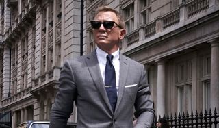 No Time To Die Daniel Craig walking in a grey suit and sunglasses