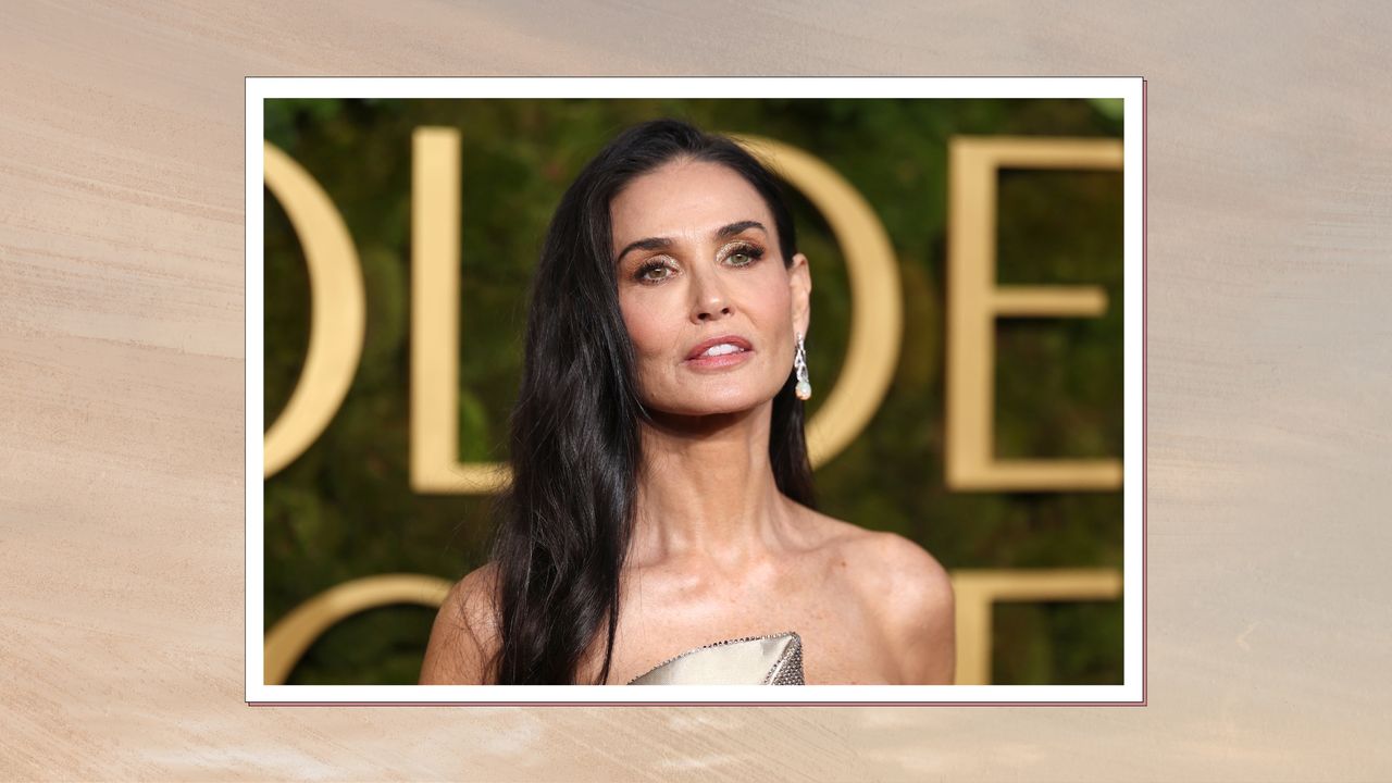 Demi Moore with side-part long brunette curly hair and wearing a strapless gold gown, on a neutral gradient background