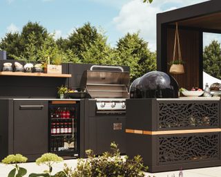 Luxe outdoor kitchen set-up in dark finish, with multiple cooking stations and drinks refrigerator.