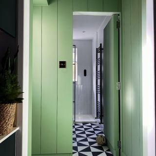 A pistachio green-painted wood-panelled hallway with a view into the bathroom with tiled black and white flooring