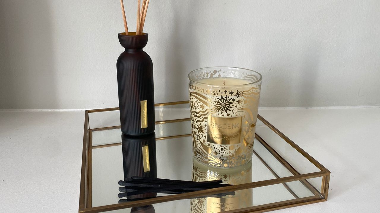 The Space NK Shimmering Spice Candle sat on a gold edged mirror tray with a black reed diffuser to the left and black matches at the front 