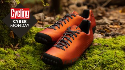 A pair of orange cycling shoes placed on a mossy log with a Cyber Monday log on the left 