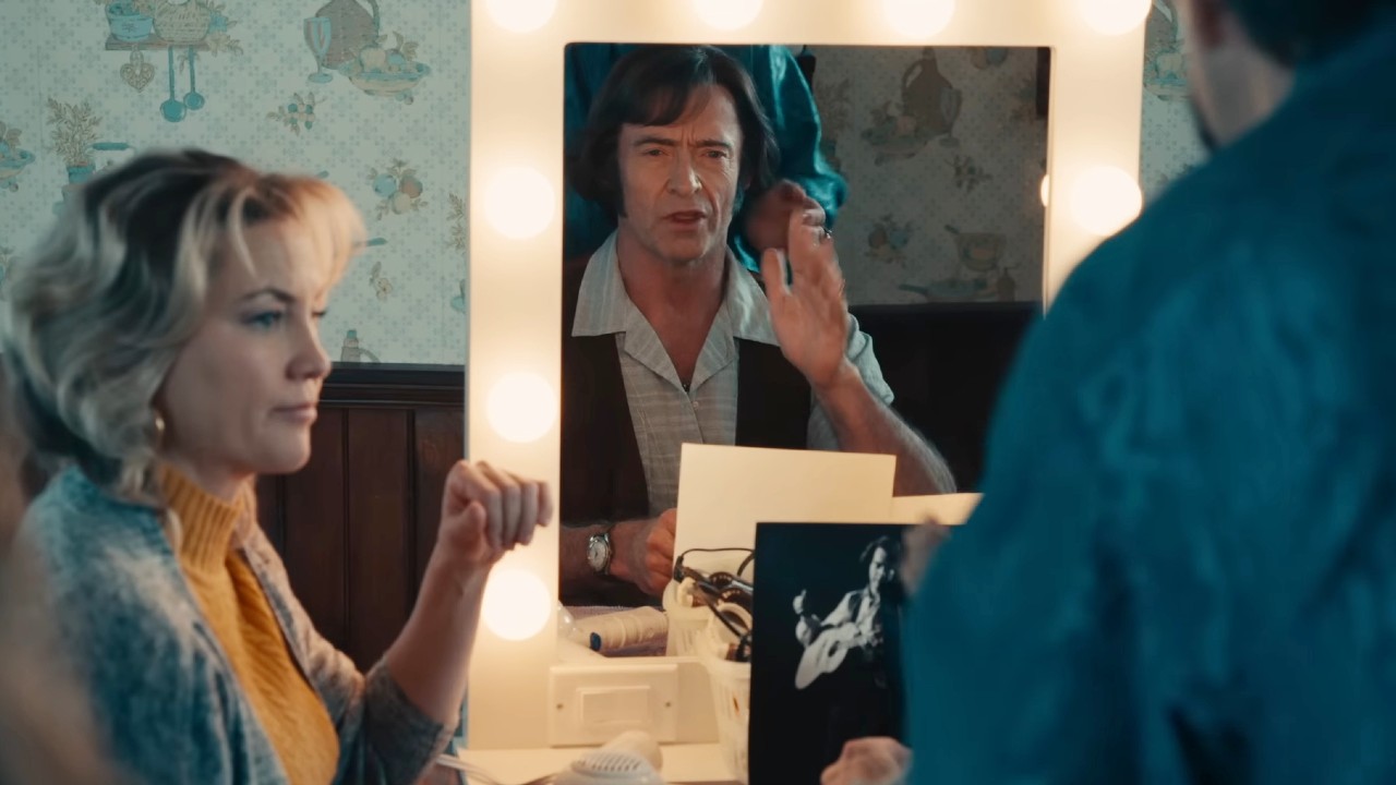 Hugh Jackman looking at the mirror with Kate Hudson looking over in Song Sung Blue.