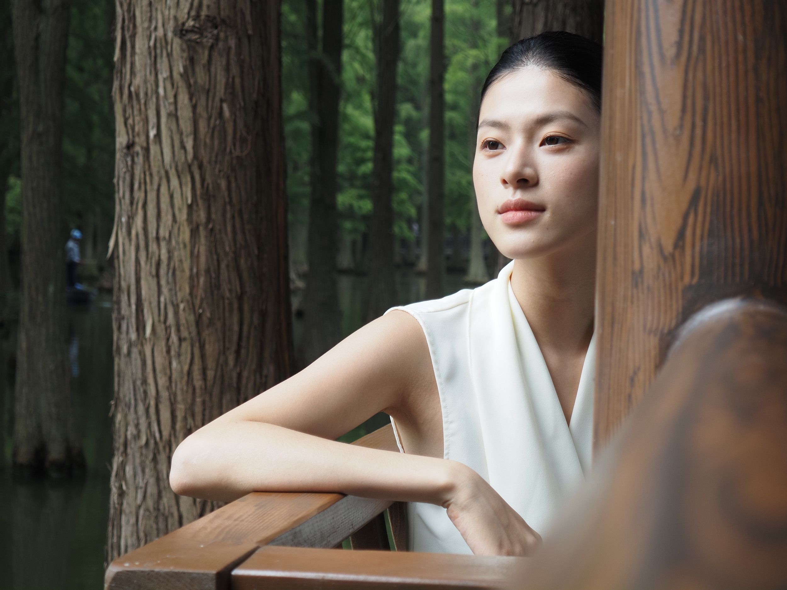 OM System PEN sample gallery: Female model in white dress leaning against a wooden barrier in a nature reserve in China