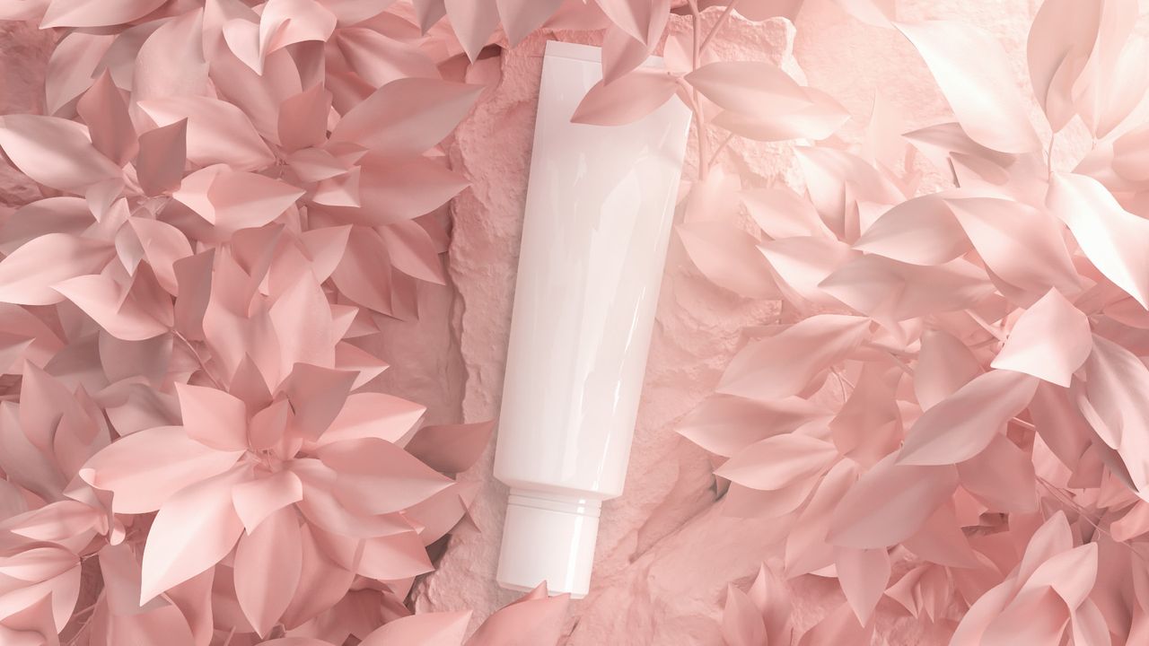 Cosmetic bottle on pink backdrop with botanical leaves