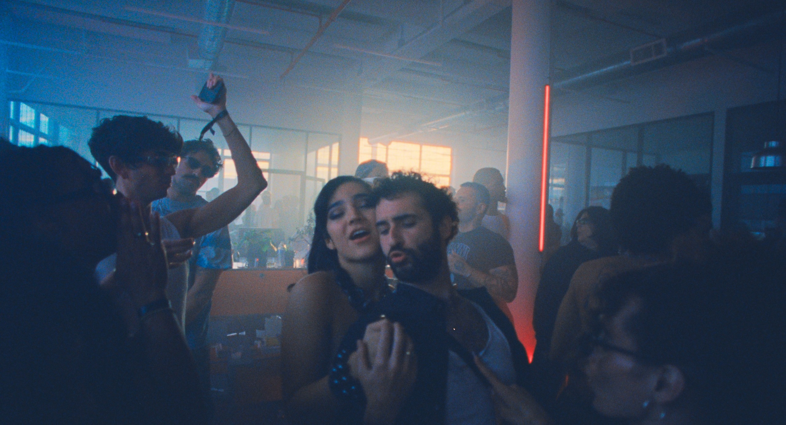 A group of people dance in a dim loft with sunshine coming through the windows, in a still from A24's 'Club Kid.'