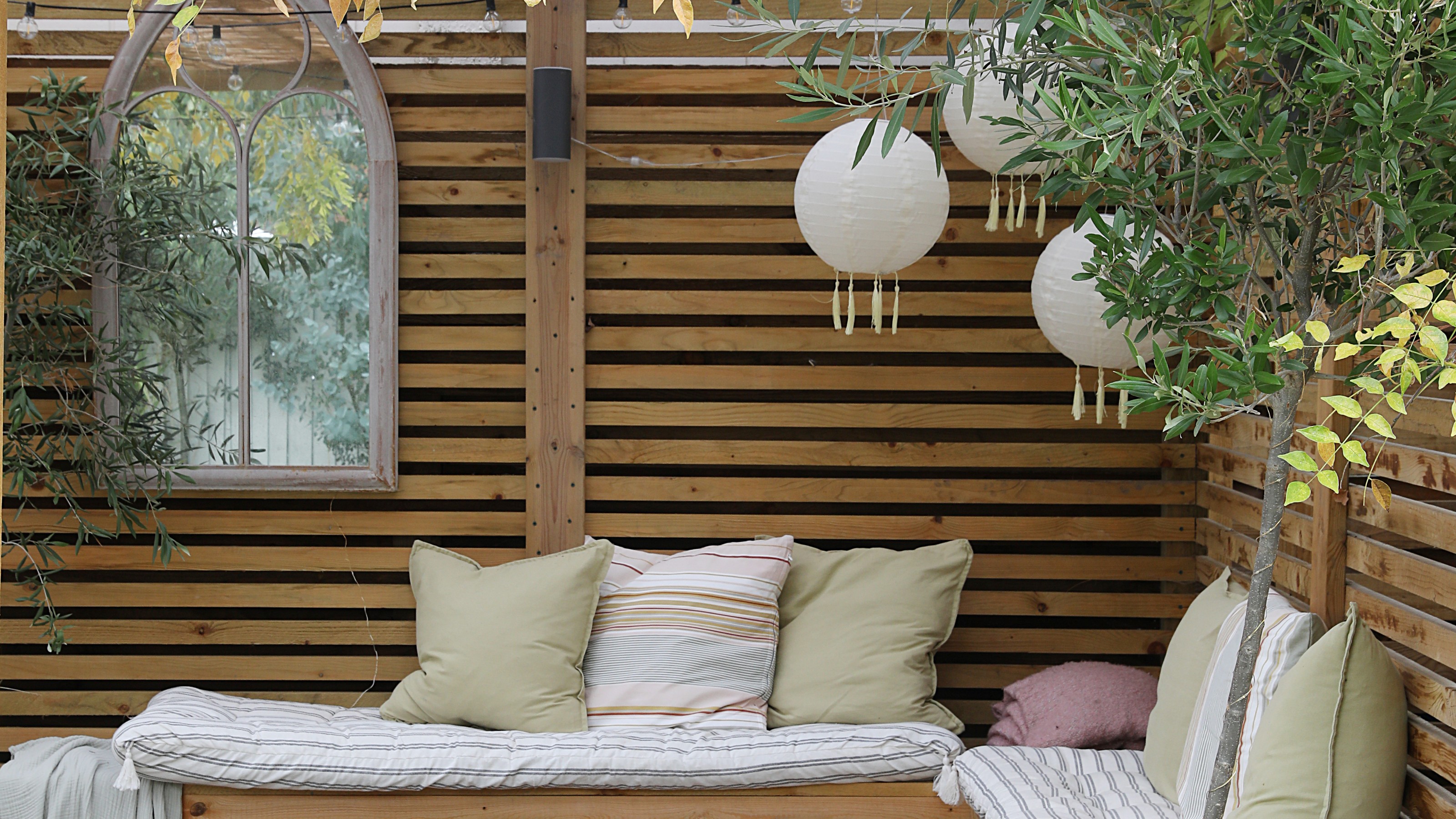 A pergola with built-in seating around a fire pit and three hanging outdoor lantern lights