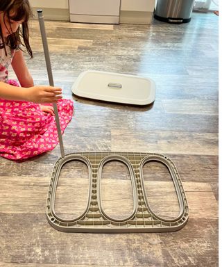 The components of the laundry organizer on my gray laminate kitchen floor and my daughter pictured to the side adding a vertical element to the rounded rectangular base