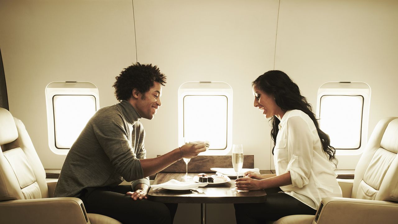 A wealthy couple eat sushi and drink champagne on a private plane.