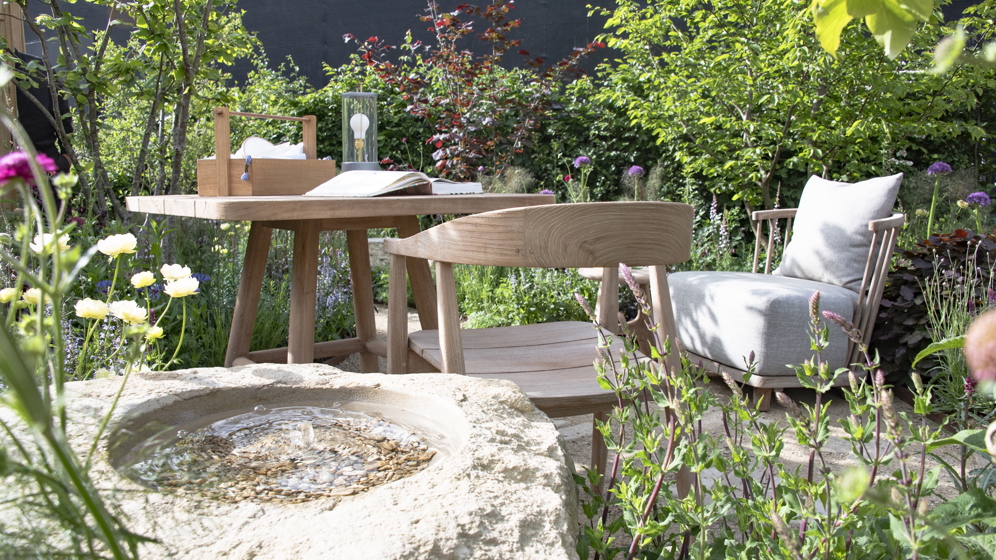 A wooden dining set at the center of a show garden at the RHS Chelsea Flower Show 2026