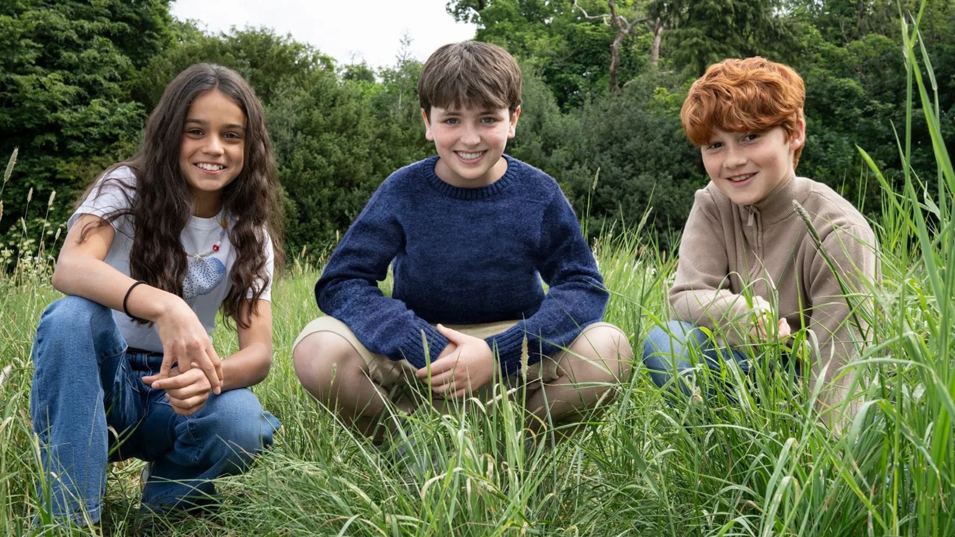 Arabella Stanton (Hermione), Dominic McLaughlin (Harry) and Alastair Stout (Ron) squat next to each other in a grassy field