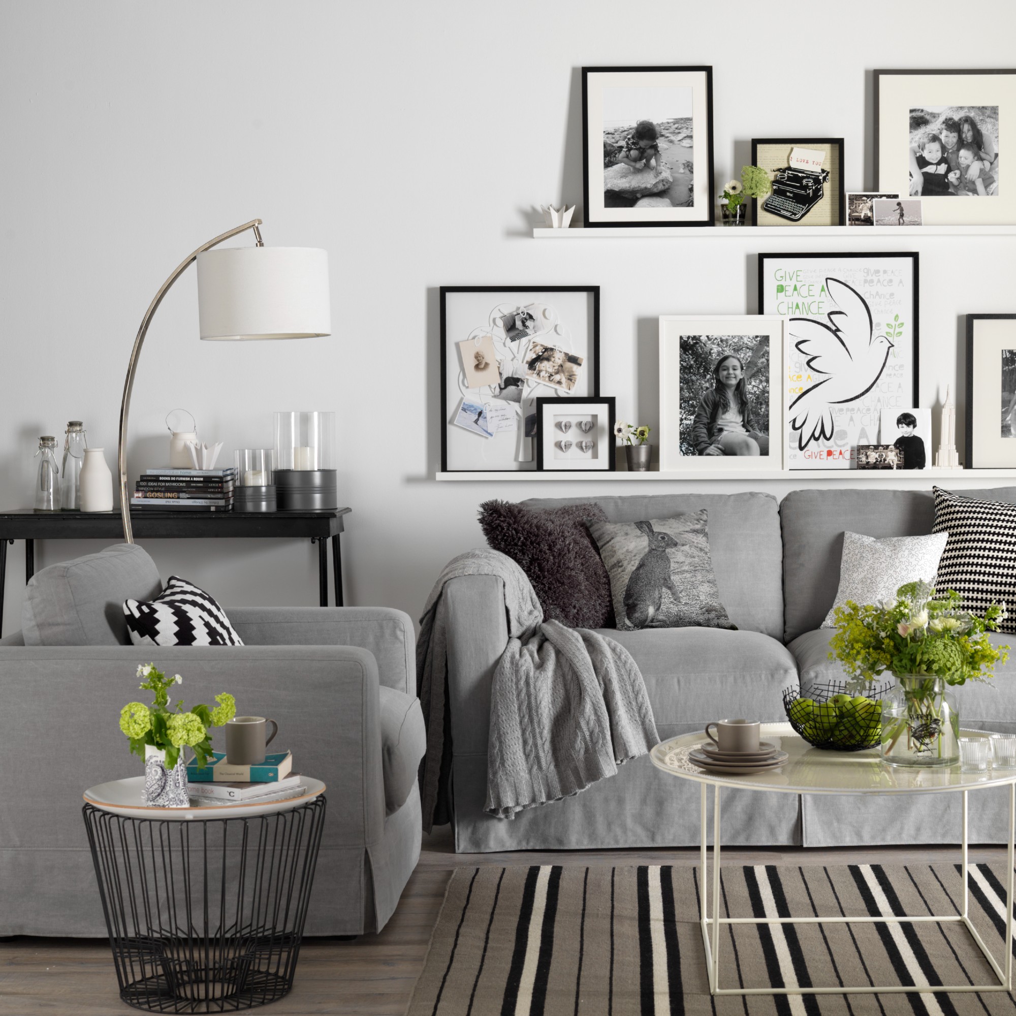 A white living room with a grey sofa and a matching armchair and a gallery wall display of photos and prints