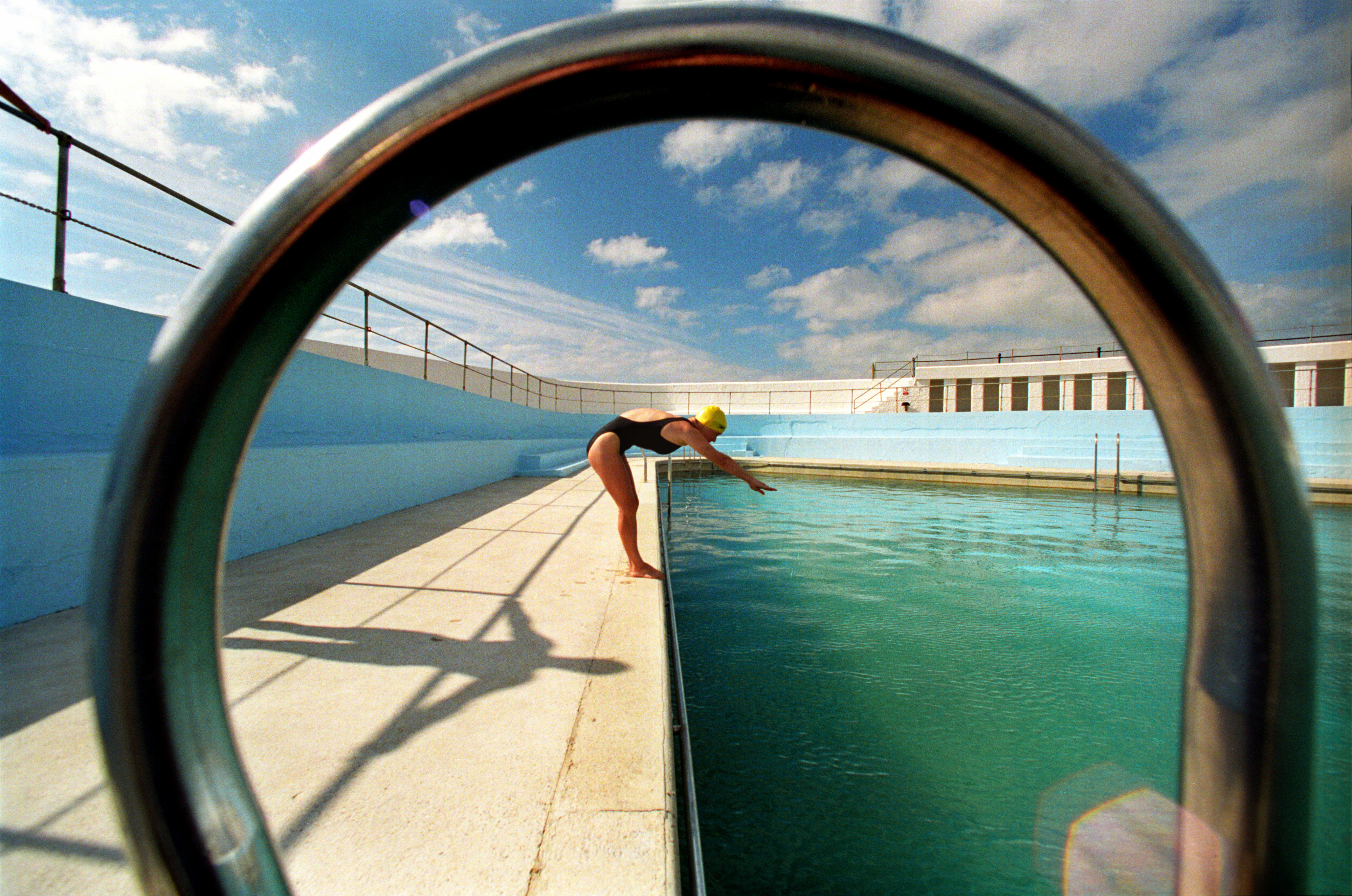 Woman diving into a triangular lido, captured through the circular ring of the ladder