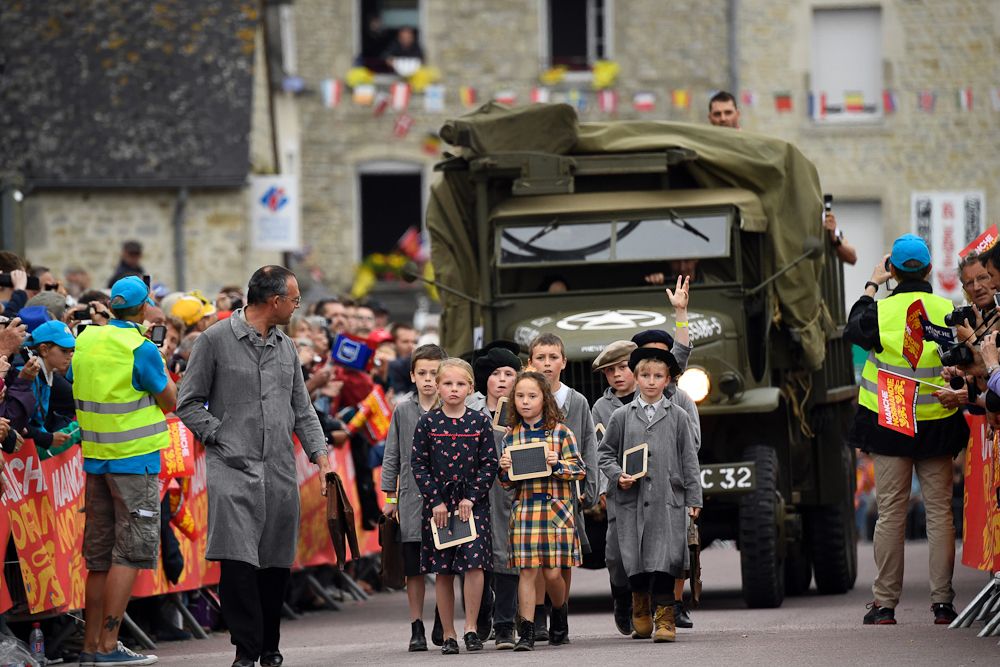 Children dressed as 1940s pupils take part in a parade, walking ahead an World War II US army vehicle during the team presentation