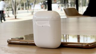 AirPods charging case on a table, resting against an iPhone X