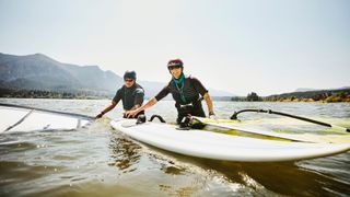 Woman standing in the sea wearing wetsuit and helmet, holding onto wind surfing board