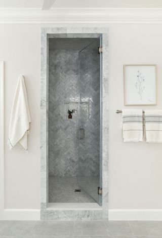 recessed alcove shower with marble details and herringbone pattern of gray opalescent tiles with white walls around and towel rail