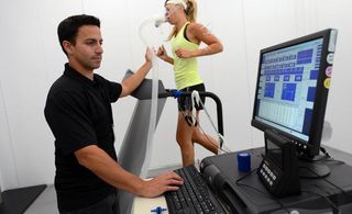 A woman wearing an oxygen mask and other medical equipment running on a treadmill