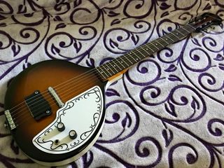 A Danelectro Baby Sitar rests comfortably on a bed often frequented by cats.