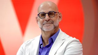 Bestselling Novelist, writer, Executive Producer, Harlan Coben in a purple shirt and white suit jacket sitting in front of a red background and smiling for the camera 