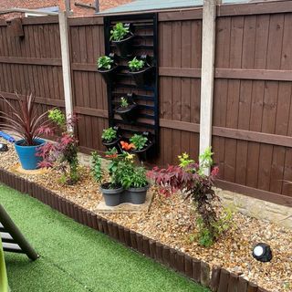 garden area with wooden wall and hanging plastic pots with plants