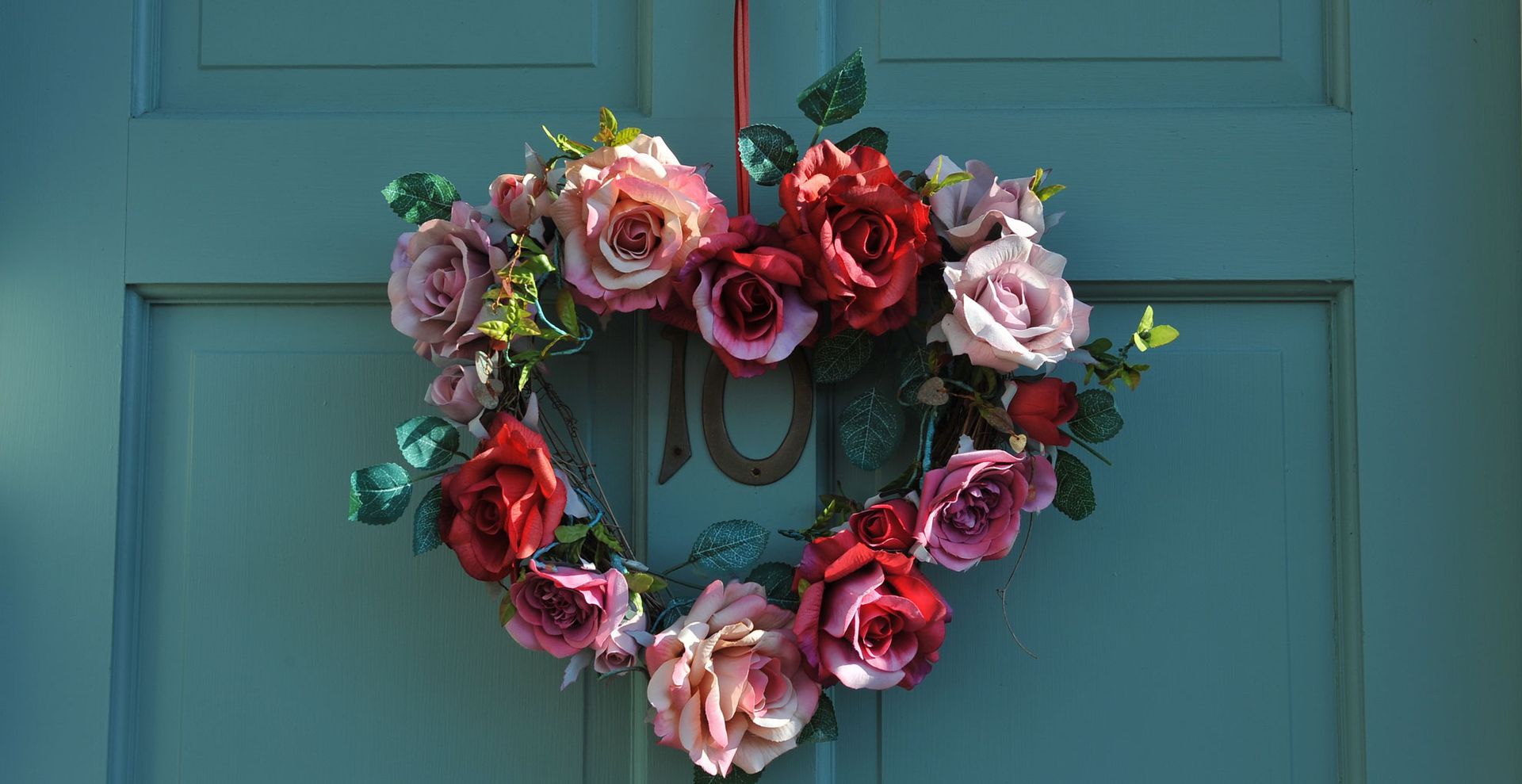 Heart-shaped flower wreath made using roses on a teal front door to show a pretty Valentine's day decoration for a home