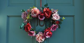 Heart-shaped flower wreath made using roses on a teal front door to show a pretty Valentine's day decoration for a home