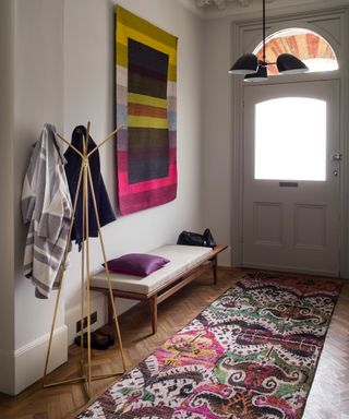 Entryway with bench and coat stand and patterned rug and wall hanging
