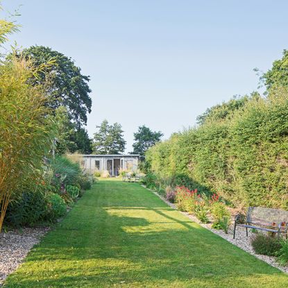 Lawn bordered by flower beds and hedges leading to garden room