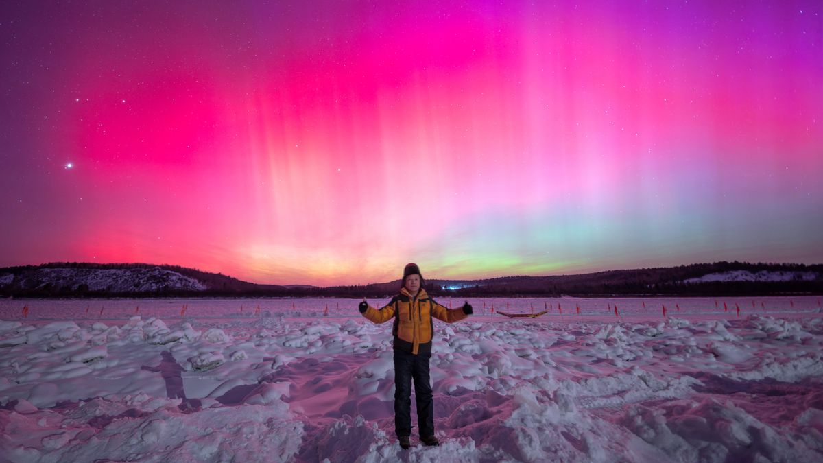 incredibly colourful aurora fill the sky with vibrant pinks and magenta. a person stands in the foreground of the image