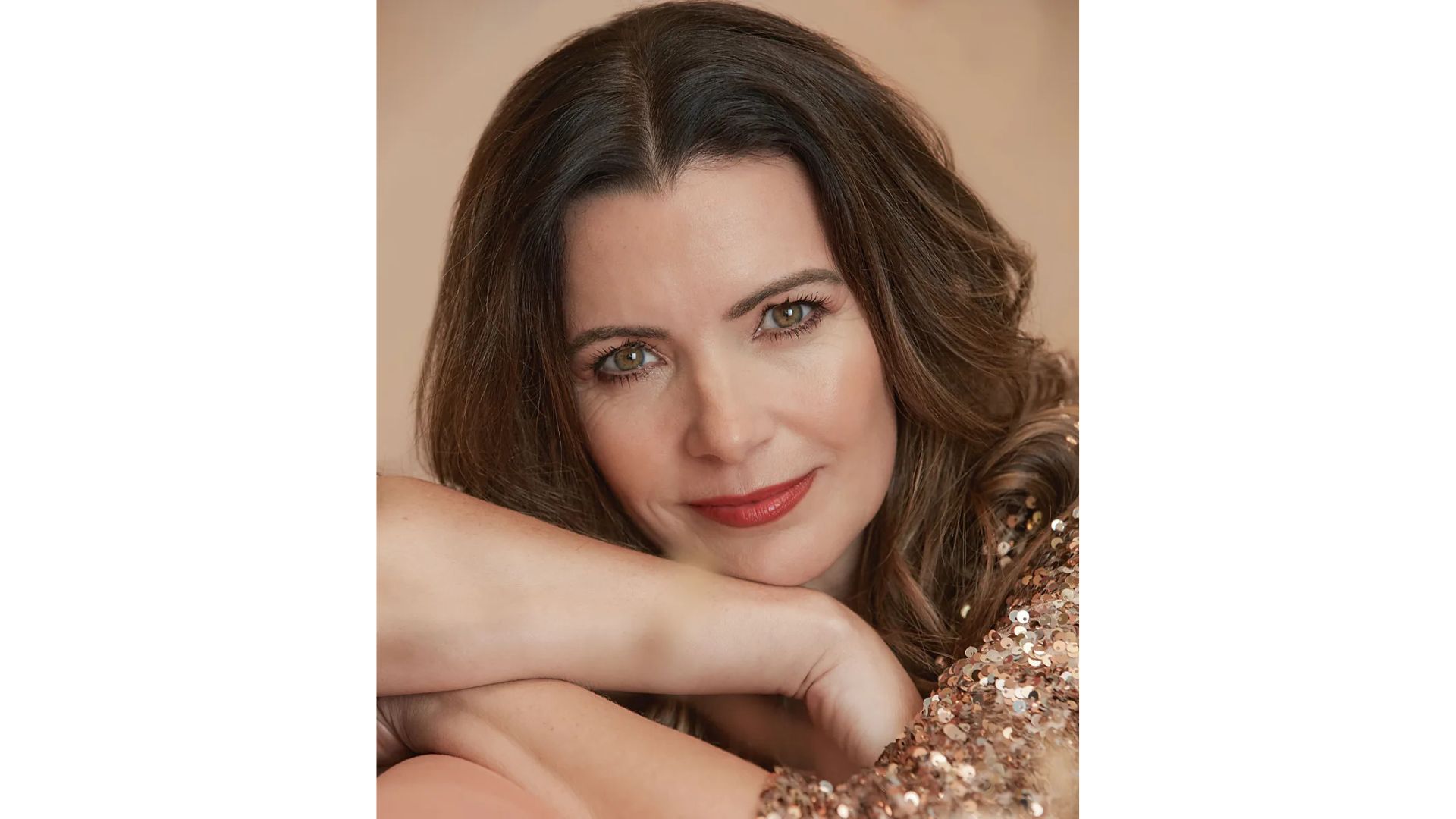 A woman with brown hair in a sequinned top wearing red lipstick